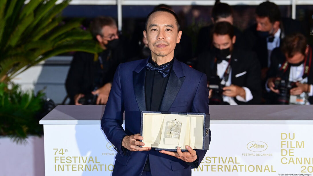 An alum in a tuxedo holds an award on the red carpet